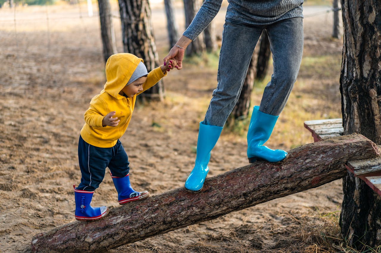 creative-01 A woman helps her toddler walk on a log in a park, showcasing child support and family bonding.